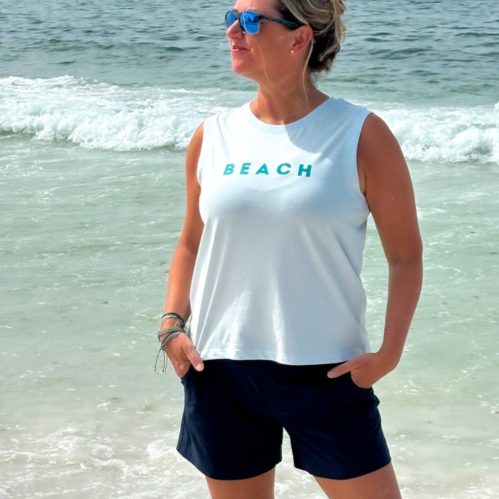 Woman wearing a light blue sleeveless shirt with 'BEACH' text at the beach.  Organic cotton apparel.  Organic cotton tank.  Womens organic cotton top.  Beach tank.  Womens Beach tank.