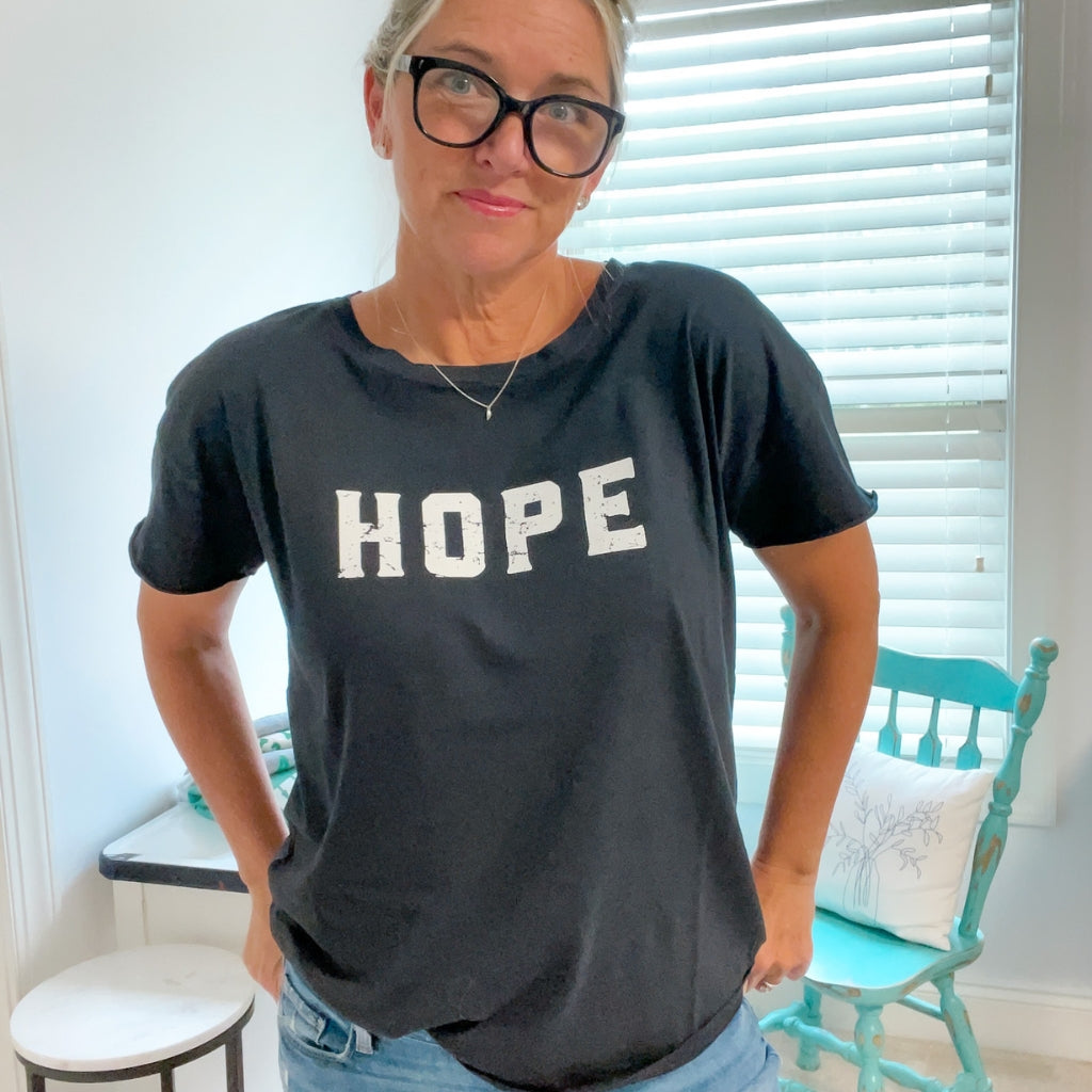HOPE printed in white ink on relaxed black cotton tshirt for women.  woman wearing black lightweight cotton tshirt saying HOPE, with jeans.