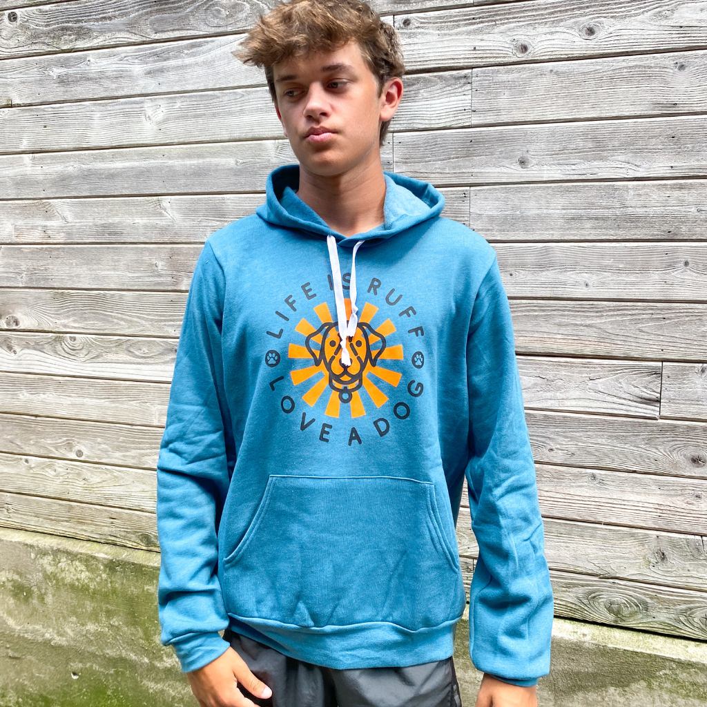 teenage guy wearing his 'life is ruff love a dog' black text saying on blue hoodie sweatshirt.  unisex hoodie sweatshirt for men & women.  dog lover hoodie.  bright orange sun with dog image in circle logo screen printed on hoodie.  young man wearing blue hoodie for dog lovers.