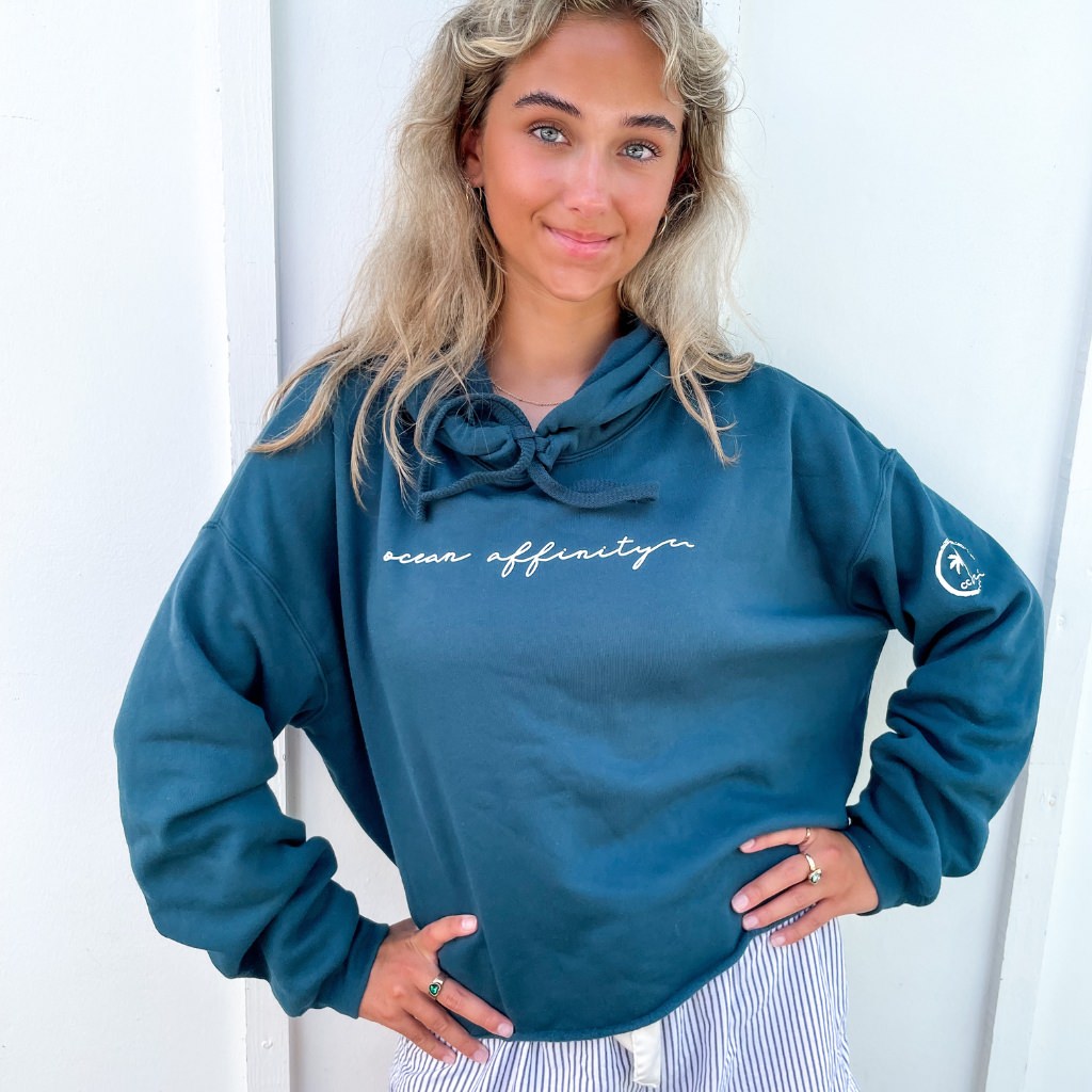 ocean affinity script white text on deep turquoise blue crop hoodie for women.  palm tree icon on sleeve.  beach apparel.  ocean lover sweatshirt.