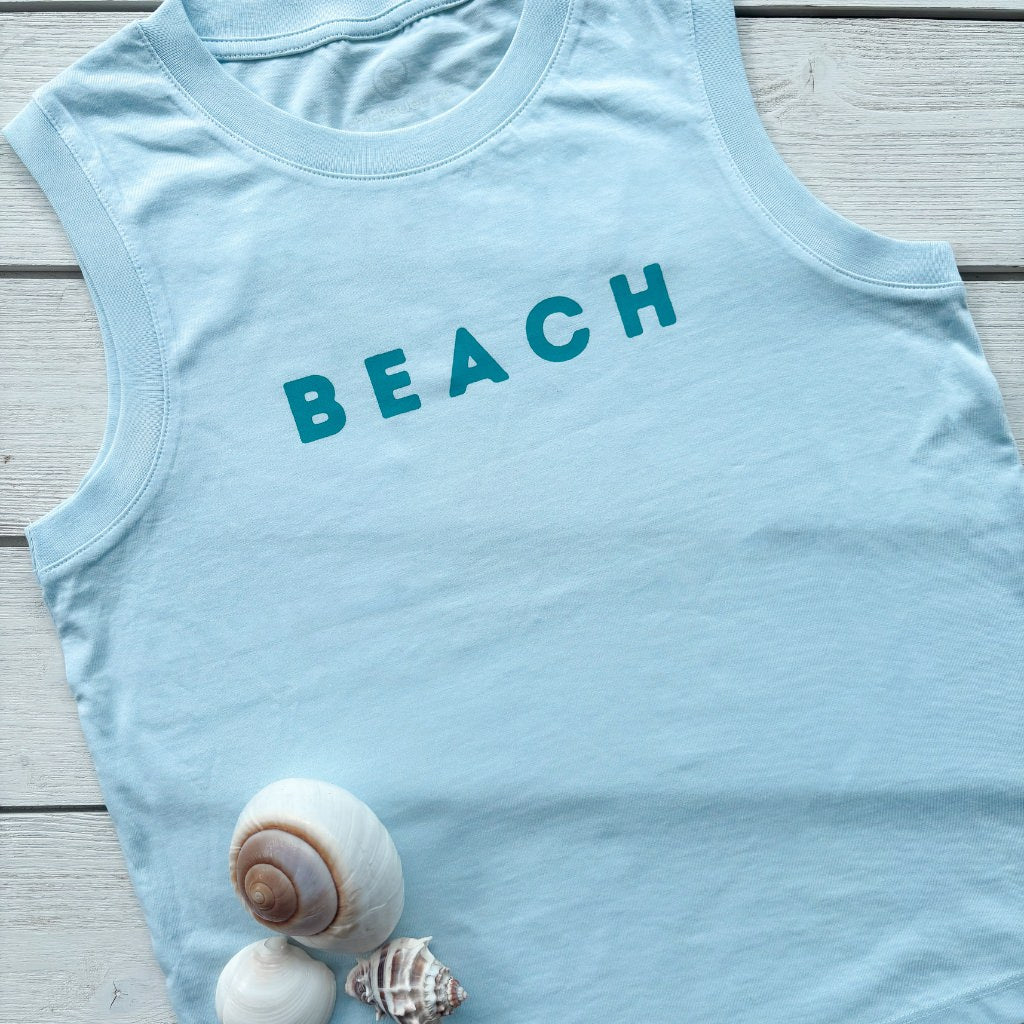 Light blue tank top with 'BEACH' text on a wooden surface with shells.  Organic cotton apparel.  Organic cotton tanks.  Womens Organic Cotton Top.