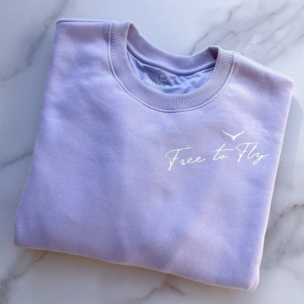 free to fly printed in white ink near the neck line of this womens lavender colored sweatshirt.  wellness apparel.  motivational sweatshirt.