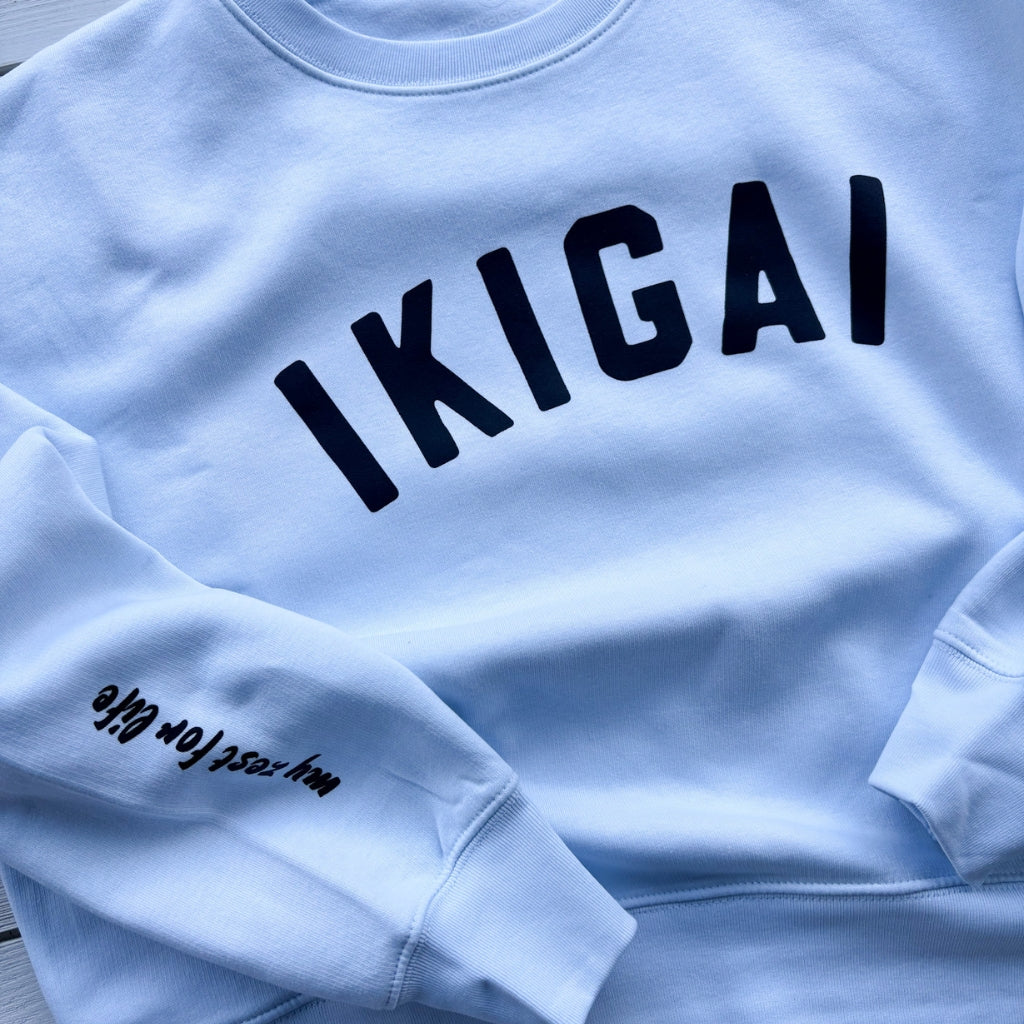 Light blue crew womens sweatshirt with black text word 'IKIGAI' on front chest. 'my zest for life' black text on sleeve.