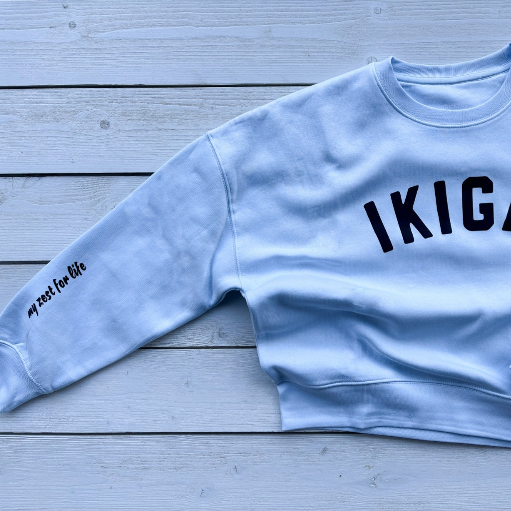 Light blue crew womens sweatshirt with black text word 'IKIGAI' on front chest. 'my zest for life' black text on sleeve.