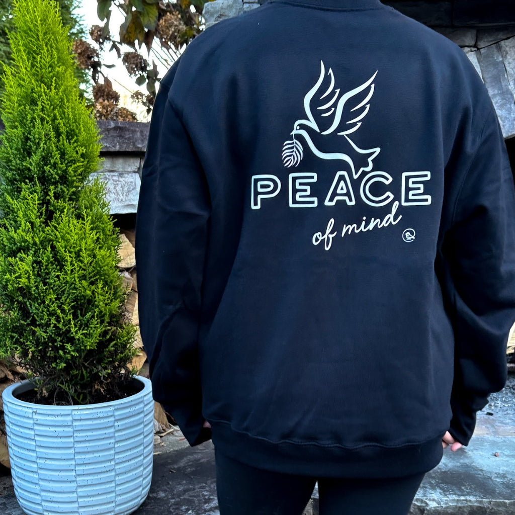 person wearing solid black crew heavyweight sweatshirt with white text 'peace of mind' on front left chest. 'peace of mind' bird graphic & text on full back print.