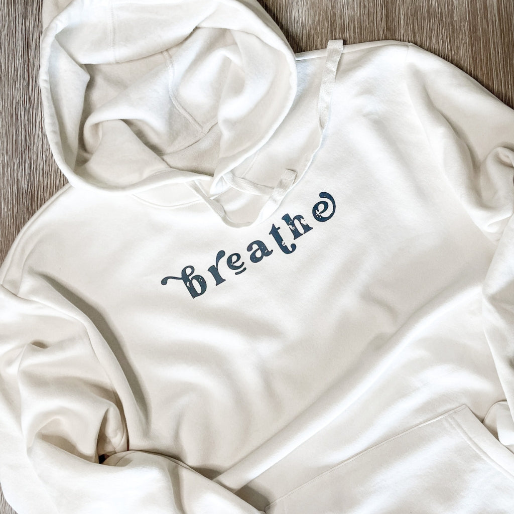 breathe. breathe hoodie simply laying on a grainy wood table. chickadee co. wellness hoodie. inspirational hoodies.