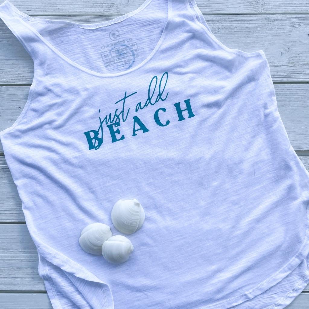 just add beach womens lightweight slub tank in white.  the words 'just add beach' on the front chest are a dark turquoise ink.