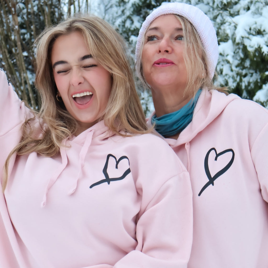 love one another hoodie.  hand drawn black heart on left chest with love one another text down sleeve on a pink hoodie.  mother and daughter wearing love one another hoodies.  pink hoodies that spread love.