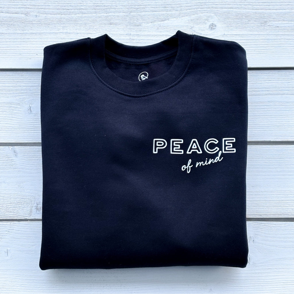 folded flatlay solid black crew heavyweight sweatshirt with white text 'peace of mind' on front left chest.  'peace of mind' bird graphic & text on full back print.