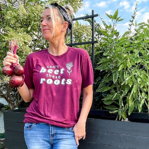 woman wearing a beet colored tshirt & jeans.  chickadee co. wellness tshirt says 'can't beet these roots' with a beet graphic picture.  