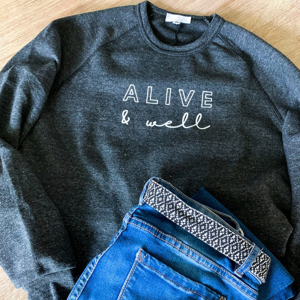 charcoal grey womens crewneck sweatshirt.  alive and well screen printed in white on the front.  super soft cozy sweatshirt.  vintage style sweatshirt.  heather grey fleece sweatshirt.  wellness sweatshirt for women.