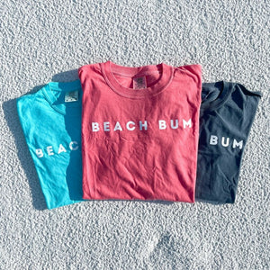BEACH BUM sweatshirts in 3 colors laying folded on the sand.  comfort colors beach t shirts.  comfort colors lagoon, watermelon, denim.