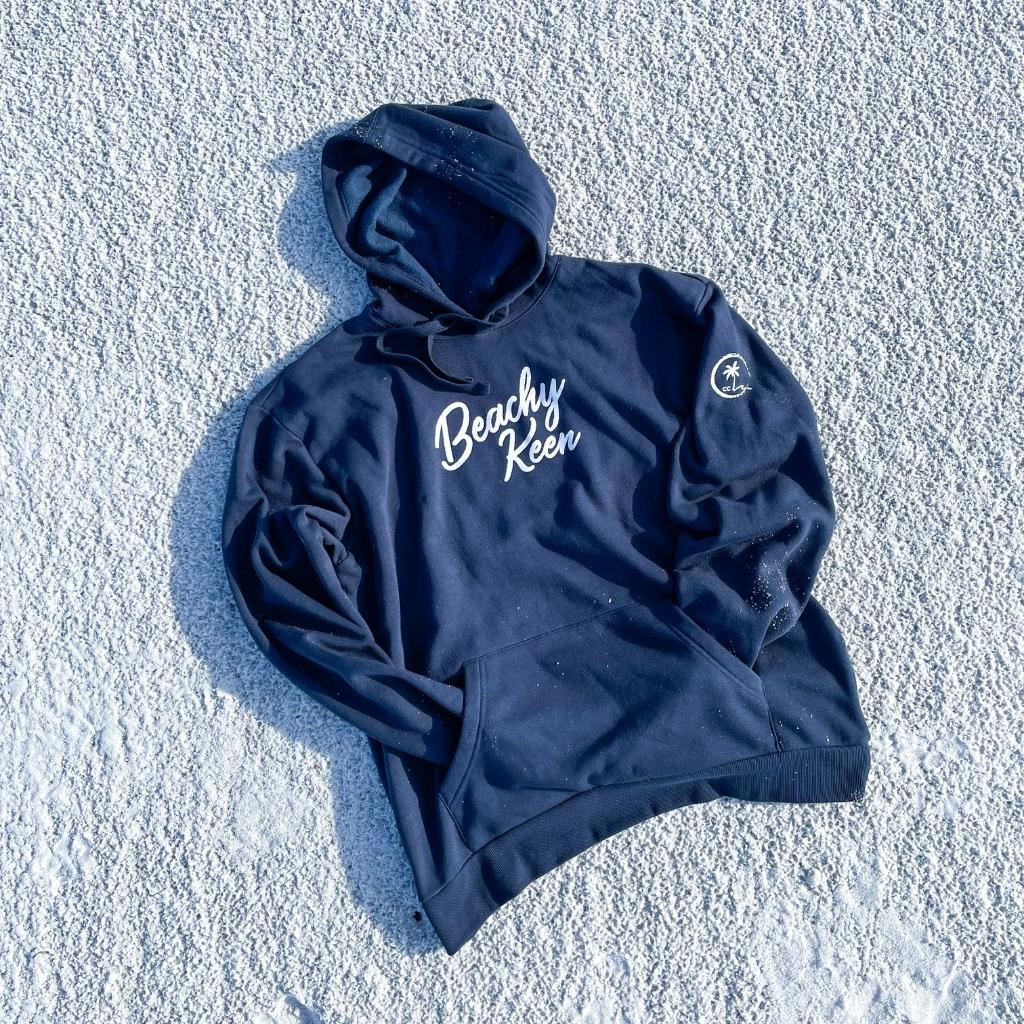 Beachy Keen hoodie.  Beach hoodie in navy color lying on the white sand.  beach hoodie.