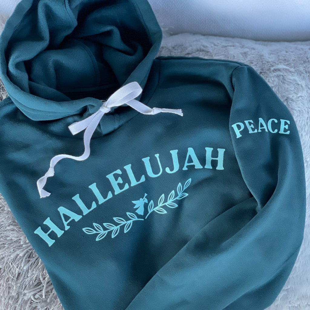 womens inspirational hoodie that says HALLELUJAH on the front with a small angel & vines under the word.  the word PEACE is on the sleeve.  super soft wellness hoodie in a deep turquoise color, with light aqua ink text & a white cotton bow in the hood. 