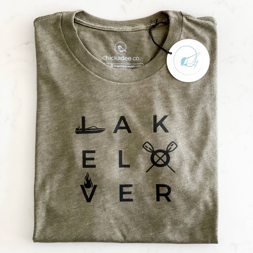 lake lover tshirt for men and women in unisex sizes.  lake lover is printed in black bold text with a boat, oars and campfire graphic.  moss colored unisex tshirt.  lake tshirt.
