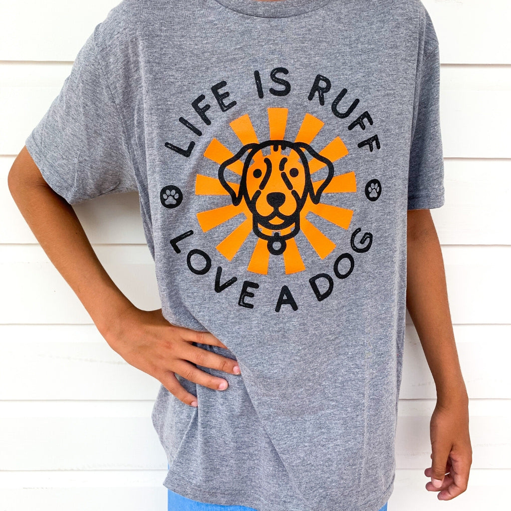 super soft vintage tshirt in grey . unisex grey triblend tshirt for men and women. dog lovers tshirt with life is ruff, love a dog quote. dog lovers tshirts. life is ruff, love a dog message. apparel for dog lovers. heather grey tshirt with black words, black dog and orange sun screen printed design on front. favorite tshirts.