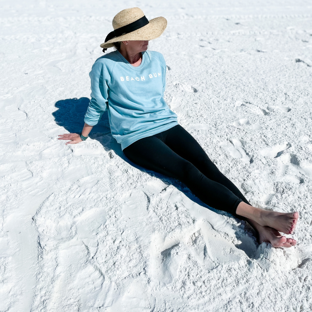 woman wearing an aqua blue crewneck sweatshirt with BEACH BUM printed in white text on the chest.  beach sweatshirts.