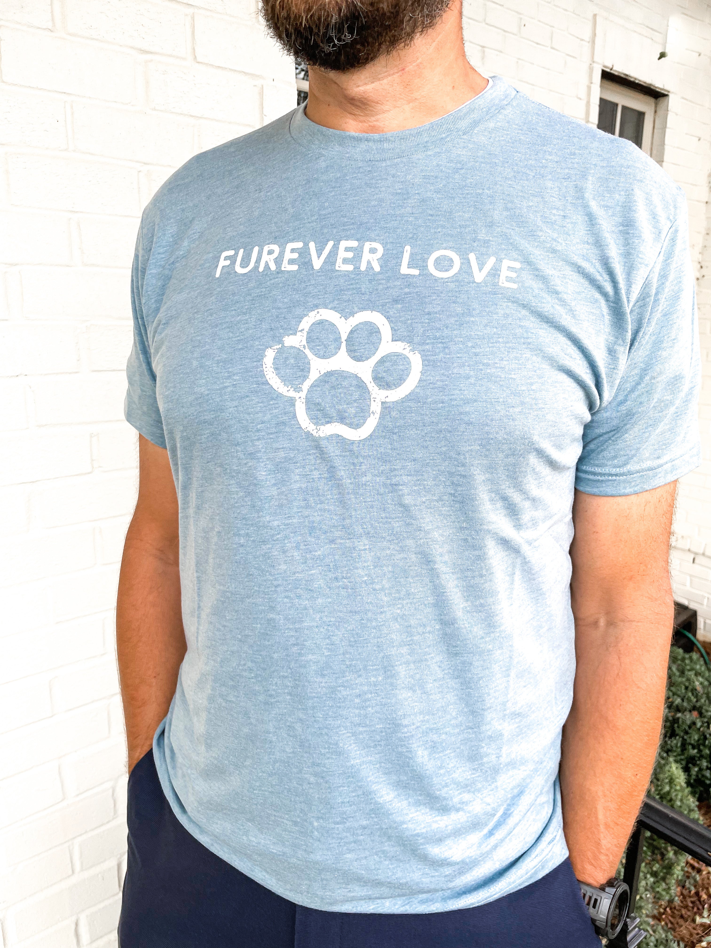 man wearing a screen printed tshirt with the saying FUREVER LOVE, and a graphic of a paw on it.  all white ink printing, on a light blue tshirt.