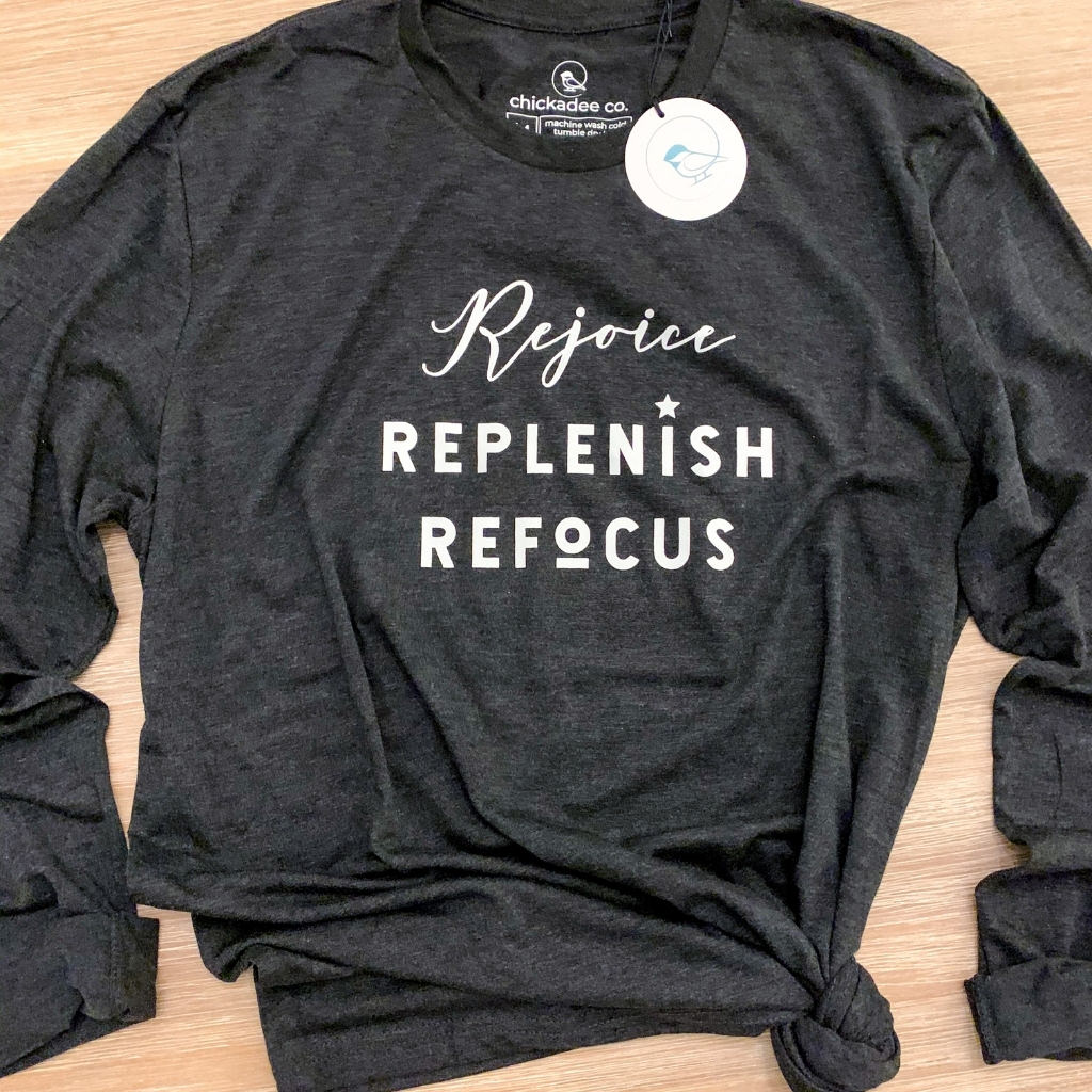 inspirational quote screen printed on t shirt saying 'rejoice.  replenish.  refocus.'  womens inspirational t shirt.  womens long sleeve crewneck t shirt.  unisex long sleeve t shirt in black.  wellness apparel for women.  relaxed fit long sleeve t shirt for women.  black and white t shirt.  workout t shirt.